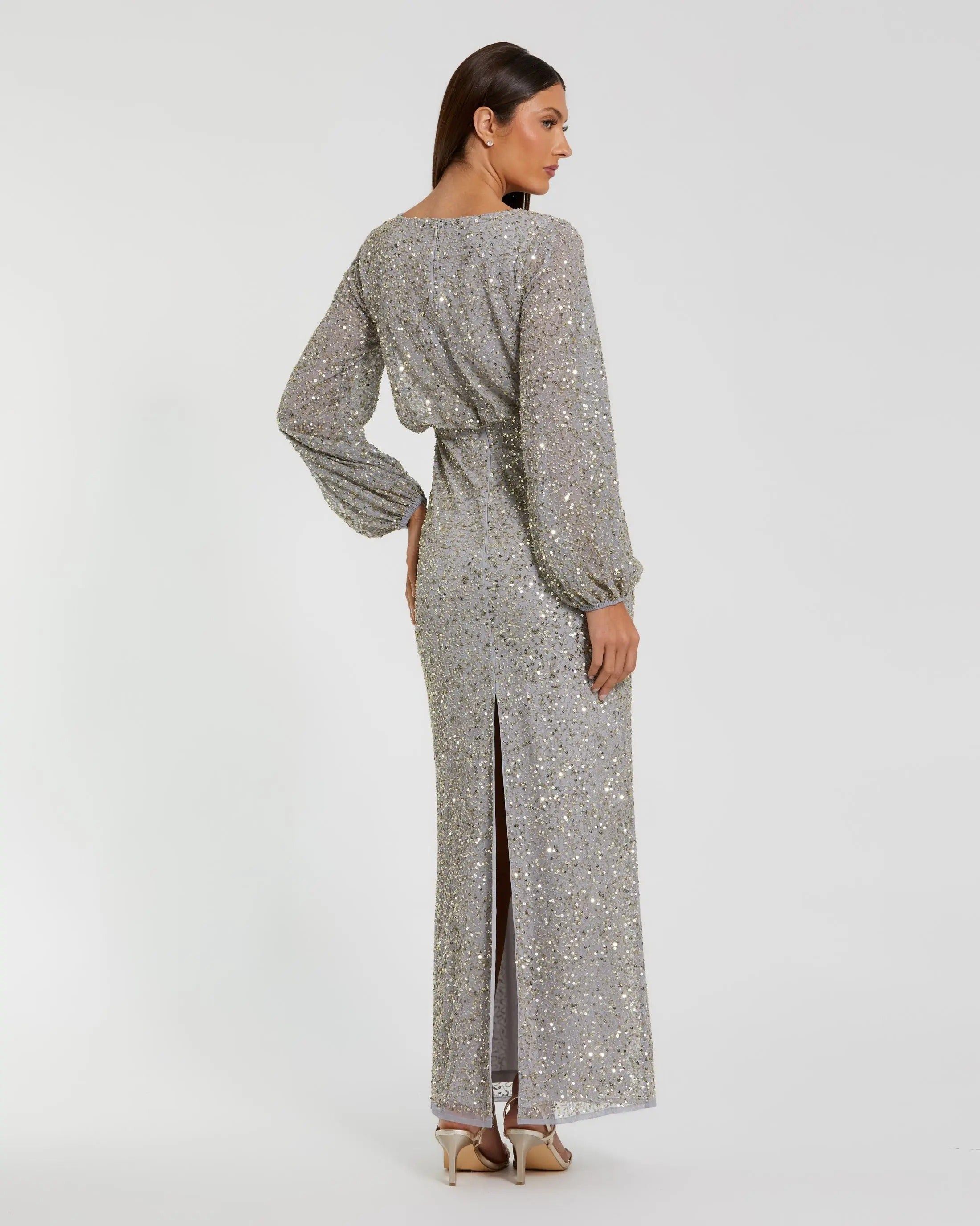 A woman models the Mac Duggal 94203 Long Formal Dress—a modest, long sequin gown with long sleeves and a back slit—paired with beige heels, as she faces away from the camera against a plain background.
